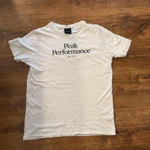 Vit Peak Performance t-shirt - Vit t-shirt från Peak Performance med svart tryck på bröstet där det står 'Peak Performance Est. 1986'. Klassisk rund halsringning och korta ärmar. Skön och enkel modell i mjuk bomull, perfekt till jeans eller shorts.