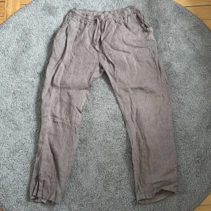 Beige linnebyxor med snörning - Snygga beige linnebyxor med elastisk midja och snörning. Byxorna har avslappnad passform, sidfickor och en bakficka. Perfekta för en chill och luftig stil under varmare dagar.