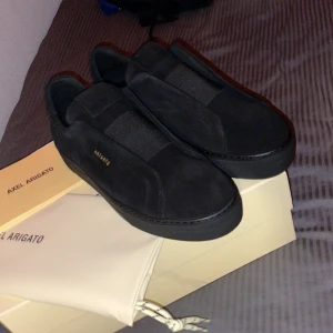 Svarta sneakers från Axel Arigato - Skirv för mer bilder !!!!Stilrena svarta sneakers från Axel Arigato i mocka med diskret logga i guld på sidan. Skorna har en minimalistisk design utan snörning och en platt sula, perfekta för en clean och modern look.