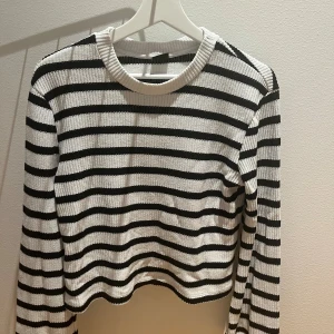 Randig stickad tröja i svart och vitt - Säljer en stickad tröja med svartvita horisontella ränder. Tröjan har rund halsringning, lång ärm och en något croppad passform. Perfekt för dig som gillar klassisk stil med en modern twist.