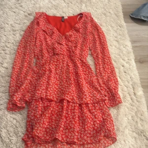 Röd blommig kortklänning H&M Divided - Superfin röd kortklänning från H&M Divided med små vita blommor, v-ringad och med långa ärmar. Klänningen har volangdetaljer och en flowy passform som ger en söt och trendig look. Perfekt för vår och sommar!