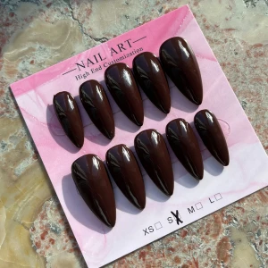 Mörkbruna lösnaglar i almondform - Säljer ett set med mörkbruna lösnaglar handgjorda i storlek S. Naglarna har en glansig finish och är formade i en snygg almondstil. Perfekt för dig som vill ha en chic och trendig look utan att behöva gå till salong.