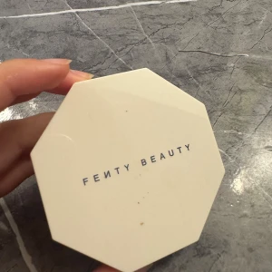 Fenty Beauty duo highlighter - Säljer en Fenty Beauty duo highlighter i en snygg oktagonformad förpackning. Ena sidan är metallic guld och andra är skimrande silver, båda med FB-loggan pressad i pudret. Perfekt för att ge ansiktet glow och highlighta kindbenen.