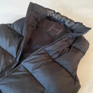 Svart dunväst från Tommy Hilfiger - Svart dunväst från Tommy Hilfiger. Passar mig, slim fit, 178cm. Typ som XS. Lite tjockare än en vanlig väst vilket gör den perfekt till lite kallare dagar..