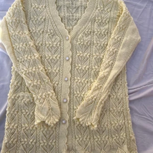 Benvitt  stickad kofta med pärlknappar - Superfin benvitt  stickad kofta med vackert mönster och pärlknappar. Koftan har lång ärm, v-ringning och detaljerade virkade kanter. Perfekt för lager-på-lager och ger en mysig vintagekänsla till din outfit.