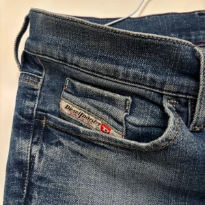 Blå Diesel LIV jeans stretch W29 - Snygga blå jeans från Diesel, modell LIV, med stretch för extra komfort. Klassisk femficksdesign, coola slitningar och kontrastsömmar. Passar dig som gillar en tidlös look med lite edge. Perfekta till sneakers eller boots.