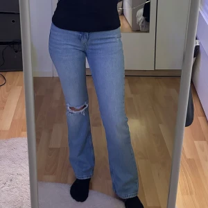 Blå bootcut jeans med slitning  - Säljer ett par ljusblå bootcut jeans med låg midja och snygg slitning på ena knät. Jeansen är i mycket bra skick, knappt använda och helt utan skador. Köparen ansvarar för frakten 