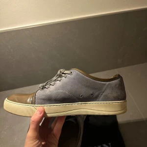 Grå sneakers från Lanvin storlek 43 - Lanvin tvåfärgad. Skosnöret trasigt på ena skon. Kostar typ 200kr nytt. Det är knutet längst fram så det syns knappt.