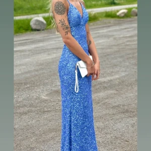 Blå balklänning  - Säljer nu min vackra balklänning! Använd endast under baldagen. Det är den perfekta blå nyansen, full med paljetter, vaddering vid bysten (bh behövs alltså inte), figurnära passform, samt en vacker korsning i ryggen där banden även är justerbara!! Skriv privat ifall fler bilder önskas! Nypris: 4.990kr, köpt via dressroomstudio på Instagram. Man får självklart med klädöverdraget samt galgen. Klänningen är uppsydd hemma efter min längd (165cm + klack på 5cm), enkelt att sprätta upp utan märken! 