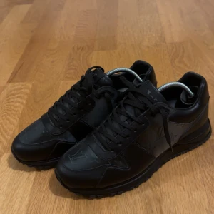 Svarta Louis Vuitton sneakers i skinn - Snygga svarta sneakers från Louis Vuitton med monogramdetaljer på ovansidan och sidorna. Skorna har rund tå, platt sula och snörning. Tillverkade i skinn med diskret glans och klassisk LV-logga. Kvitto och box medföljer
