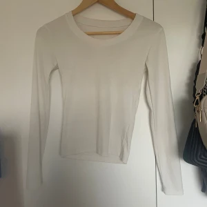 Vit långärmad topp i bomull - Säljer en enkel och stilren vit långärmad topp i mjuk bomull. Modellen har rund halsringning och en slim passform som sitter snyggt på kroppen. Perfekt att matcha med jeans eller kjol för en clean look.