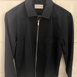 Svart overshirt från J. Harvest & Frost - Stilren svart overshirt med klassisk krage och silverfärgad dragkedja framtill. Har en enkel bröstficka och raka linjer för en clean look. Materialet känns mjukt och lätt, perfekt för lager-på-lager. Långärmad modell som funkar till många stilar.