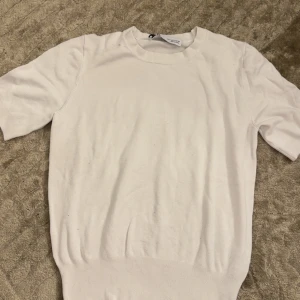 Vit stickad kortärmad tröja - Säljer en stilren vit stickad tröja från COS med korta ärmar och rund hals. Tröjan har en klassisk passform och ribbade detaljer vid ärmslut och nederkant. Perfekt för lager-på-lager eller sommarens svalare dagar. Priset kan diskuteras