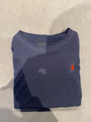 Två Polo Ralph Lauren t-shirts - Säljer två klassiska t-shirts från Polo Ralph Lauren. En är marinblå med röd logga och en är olivgrön med mörkblå logga. Båda har rund hals och är gjorda i mjuk bomull. Perfekta för en clean och stilren look.
