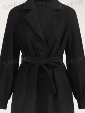 Svart kappa med knytskärp från SHEIN - Stilren svart kappa från SHEIN med klassisk krage, knappar framtill och ett matchande knytskärp i midjan. Kappan har långa ärmar och en rak passform som ger en snygg siluett. Perfekt för dig som gillar minimalistisk och trendig stil.