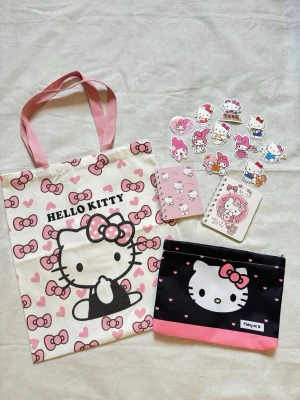 Hello Kitty Tote + mindre väska + 2 anteckningsblock + klistermärken  - Söt shoppingväska med Hello Kitty-motiv i vitt och rosa, dekorerad med hjärtan och rosetter. Mindre väska följer med och 2 anteckningsblock med klistermärken. Perfekt för dig som älskar kawaii och vill ha en unik accessoar med ikonisk design.