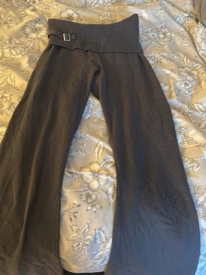 Mörkgrå mjukisbyxor med ribbad midja - Mörkgrå mjukisbyxor med bred ribbad midja och dekorativt spänne. Byxorna har raka, vida ben och är gjorda i ett mjukt, stickat material som känns riktigt skönt. Perfekta för en avslappnad och chill stil.