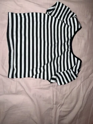 Svartvit randig croppad topp - Säljer en svartvit randig croppad topp med korta ärmar och rund hals. Helt öppen i ryggen. Toppen har en tight passform och är perfekt för dig som gillar en enkel men snygg stil. Materialet känns mjukt och stretchigt, troligen bomull eller polyester.