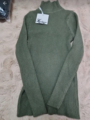 Olivgrön ribbstickad tröja  - Snygg olivgrön ribbstickad polotröja från Kuluwear. Tröjan har lång ärm, hög krage och är tillverkad i ett mjukt, stretchigt material som sitter tajt mot kroppen. Perfekt för lager på lager och enkel att matcha med jeans eller kjol.