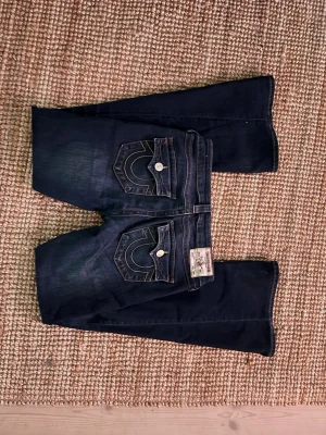 Mörkblå True Religion jeans Joey - Säljer ett par bootcut mörkblå jeans från True Religion med snygga bakfickor. Innerbenslängden är ca 83cm! Färgen är lite urtvättad jämfört från när de var nyköpta, men annars inga andra defekter! (Köpta för 1 299kr)
