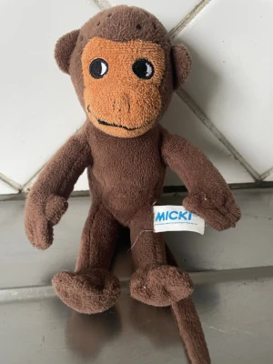 Herr Nilsson  mjukisapa från Micki - Herr Nilsson Söt brun mjukisapa från Micki med ljusbrunt ansikte och broderade ögon. Tillverkad i mjukt tyg och har en lång svans. Perfekt som gosedjur eller dekoration.