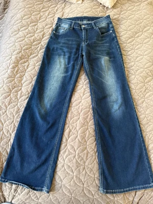 Blå bootcut jeans med slitningar - Snygga blå bootcut jeans med lätt slitna detaljer framtill och bakficka. Jeansen har klassisk femficksdesign, normal midja och vida ben. Perfekta för dig som gillar en avslappnad och trendig look.