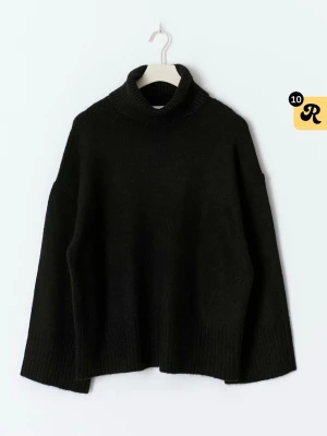 Svart polotröja i stickat material - Mysig svart stickad polotröja med breda ärmar och ribbade muddar. Tröjan har en avslappnad passform och hög polokrage som ger extra värme. Perfekt för kalla dagar och enkel att matcha med olika outfits.