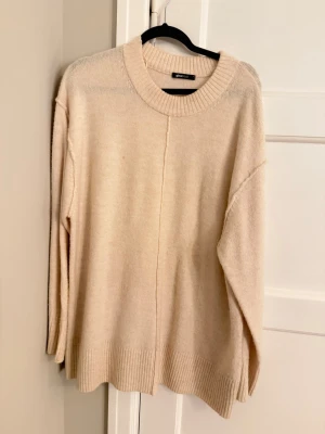 Beige oversized stickad tröja Gina Tricot - Beige oversized stickad tröja från Gina Tricot med rund halsringning och markerad söm framtill och baktill. Tröjan har långa ärmar, nedhasade axlar och bred ribbstickning vid ärmslut och nederkant. Perfekt för lager på lager och enkel att styla. Passar s-m också oversized 
