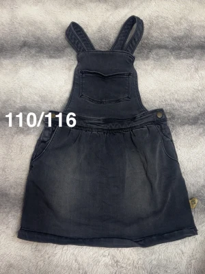 Mörk jeanskjol med hängslen - Snygg jeanskjol med hängslen och bröstficka. Kjolen har knappdetalj i midjan och två sidofickor. Perfekt för en avslappnad och trendig look.🌸Fint använt skick. Strechigt och mjukt material. Storlek 110/116