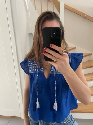 Blå  blus från H&M - Snygg blå blus från H&M med vita broderier framtill. Nyskick, endast använd 1 gång! 