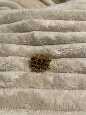 Guldig ring med nitar - Cool ring i guldfärgad metall med dubbla rader av spetsiga nitar runt hela ringen. Ringen har en chunky och edgy design som verkligen sticker ut och ger en tuff vibe till din stil.