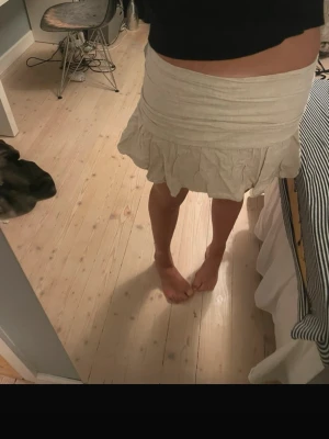 Beige volangkjol med omlottkänsla i linne med inbyggda shorts  - Säljer en söt beige kortkjol med volangkant och omlottkänsla i linne med inbyggda shorts . Kjolen har en lätt och luftig passform, perfekt för varmare dagar. Enkel att matcha med olika toppar för en trendig look.