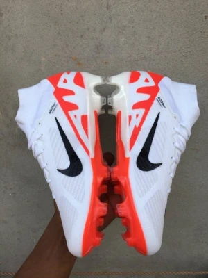 Nike Zoom vitt löparspikskor - Säljer ett par Nike Zoom löparspikskor i vitt med svarta swoosh-loggor och coola orange detaljer. Skorna har en aerodynamisk form och är designade för maximal fart på löparbanan. Ovandelen är i mesh för bra ventilation och sulan har spikar för extra grepp.