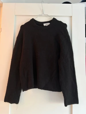 Svart stickad tröja från Gina tricot - Mysig svart stickad tröja från Gina tricot med rund halsringning och långa ärmar. Tröjan har en avslappnad passform och ribbade muddar vid ärmslut och nederkant. Perfekt för kalla dagar och enkel att matcha med olika outfits.
