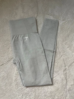 Grå leggings från Gymshark - Snygga ljusgrå leggings från Gymshark med hög midja och diskret mönster längs benen. Två små fläckar framtil. Stretchigt material som sitter skönt och formar sig efter kroppen. Perfekta för träning eller chill. Gymshark-logga på höften.