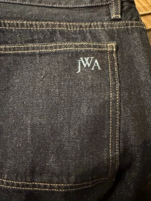 Mörkblå jeans från JWA - Snygga mörkblå jeans från JWA med klassisk femficksdesign och kontrastsömmar. Jeansen har en rak passform och är tillverkade i denim. Perfekta för dig som gillar stilrena och tidlösa plagg.