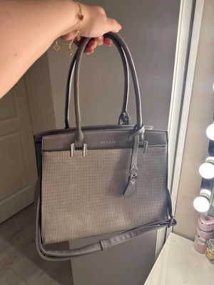 Grå väska - handväska  - Säljer en fin grå handväska med silver detaljer som inte kommer till användning mer. Bandet har släppt sin tråd och därför har den öppnat sig, utan det så är väskan i gott skick. Går enkelt att sy ihop ifall man har möjlighet till de.