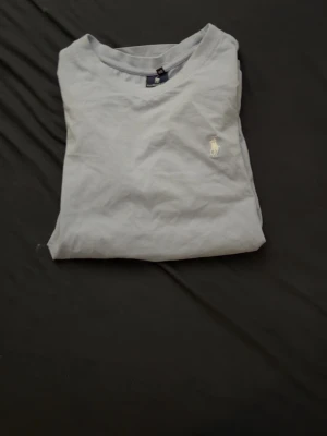 Ljusgrå t-shirt från Ralph Lauren - Snygg ljusgrå t-shirt från Ralph Lauren med klassisk passform och rund hals. T-shirten har en liten broderad logga på bröstet och är tillverkad i mjuk bomull. Perfekt för en clean och stilren look.
