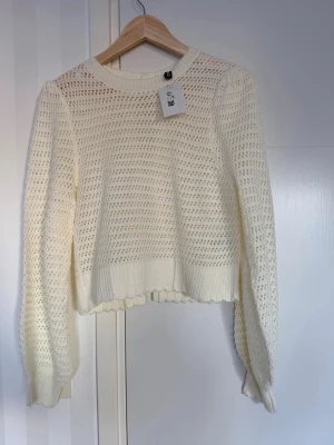 Vit stickad tröja med rosetter - Söt vit stickad tröja från H&M med hålmönster och två dekorativa rosetter i ryggen. Tröjan har lång ärm, ribbade muddar och en lätt croppad passform. Perfekt för dig som gillar en romantisk och trendig stil.