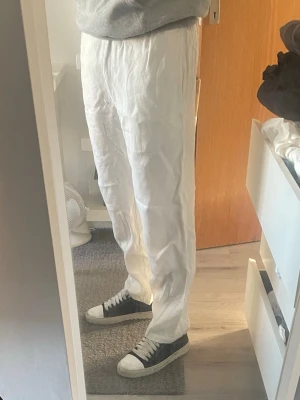 Vita linnebyxor med avslappnad passform - Säljer ett par vita linnebyxor med avslappnad passform. Byxorna har resår i midjan och är tillverkade i ett lätt och luftigt linnetyg, perfekta för en chill och stilren look. Nypris: runt 600kr