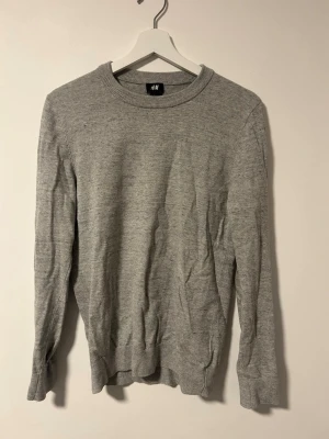 Ljusgrå stickad tröja från H&M - En enkel och stilren ljusgrå stickad tröja från H&M. Tröjan har rund halsringning, långa ärmar och ribbade muddar vid ärmslut och nederkant. Tröjan är väldigt elastisk och kan även passa S. Pris kan diskuteras. Fler bilder kan skickas vid behov.