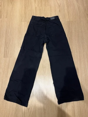 Svarta vida jeans från Gina Tricot - Säljer ett par svarta jeans med raka, vida ben och klassisk femficksmodell. Jeansen har medelhög midja. Perfekta för en avslappnad och trendig stil.