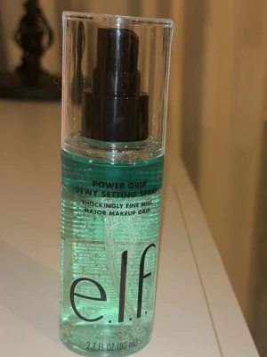 e.l.f. Power Grip Dewy Setting Spray - Fräsch face mist från e.l.f. i en genomskinlig plastflaska med svart spraymunstycke. Innehållet är ljusblått och ger en dewy finish som håller sminket på plats hela dagen. Perfekt för att fräscha upp huden och få en glowig look.
