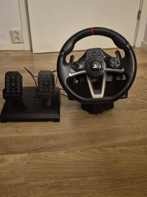 Playstation ratt och pedaler - Säljer en Playstation racingratt med pedaler, perfekt för PlayStation 4 och 5 . Ratten har svart konstläder, metallspakar och flera knappar för full kontroll. Pedalerna är i svart plast och metall, med gummigrepp för stabilitet. Grymt för racing och simracing! Ratten kommer med spelet  "The crew 2" 