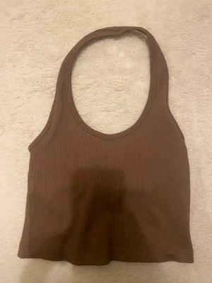Brun ribbad linnetopp från Gina Tricot - Snygg brun ribbad linnetopp från Gina Tricot. Toppen är ärmlös med rund halsringning och croppad passform. Perfekt att styla med jeans eller kjol för en trendig look.