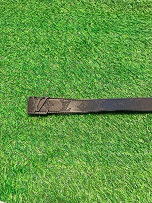 Svart Louise Vuitton bälte med monogram - Snyggt svart bälte från Louise Vuitton med klassiskt L.V-spänne och diskret monogrammönster längs hela remmen. Bältet är gjort i läder och har en stilren, modern look som passar till många outfits.