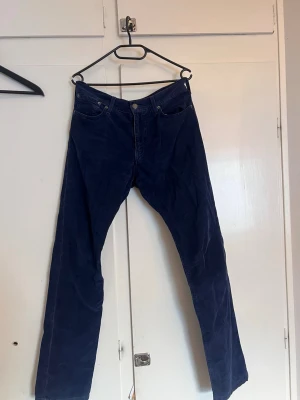 Mörkblå manchesterbyxor - Mörkblå manchesterbyxor med klassisk femficksmodell och raka ben. Byxorna har tydlig manchesterstruktur och stängs med knapp och dragkedja. Perfekta för dig som gillar en retrostil och vill ha något bekvämt och snyggt.