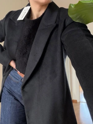 Svart oversized kappa med bred krage - Helt ny kort kappa / kavaj från NA-KD i svart i storlek 36 i ullblandning med prislappen kvar. 🖤  Jackan är i en kort modell och har en blazerdesign samt en mjuk känsla tack vare dess ullblandning. Jackan har fickor i sidsömmen, en tryckknappsstängning ner längs framsidan med en överlappande stil.