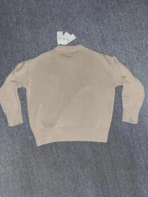 Beige stickad tröja från Ami - Snygg beige stickad tröja från Ami Alexandre Mattiussi. Tröjan har en rak passform, ribbade muddar vid ärmslut och nederkant samt rund halsringning. Perfekt för dig som gillar stilrena och klassiska plagg i mjukt material. Tröjan saknar prislapp då jag ryckte av den för jag trodde den passade mig men den är helt ny! 🙌🏼