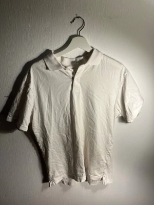 Vit pikétröja från GAP - Klassisk vit pikétröja från GAP med krage och knappar framtill. Tillverkad i mjuk bomull och har korta ärmar. Enkel och stilren design som passar till det mesta.